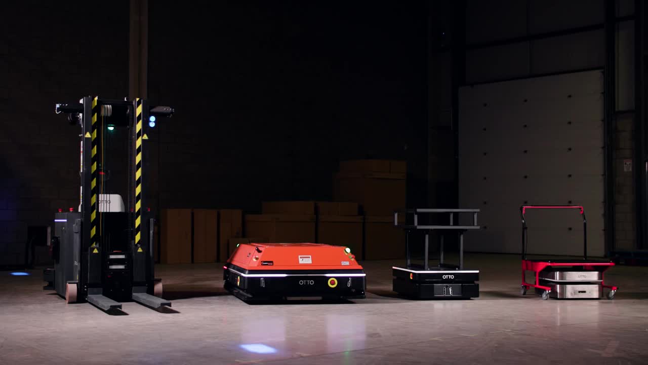 Four OTTO autonomous mobile robots side by side in a facility: a pallet lifter, a large deck robot, and two cart movers