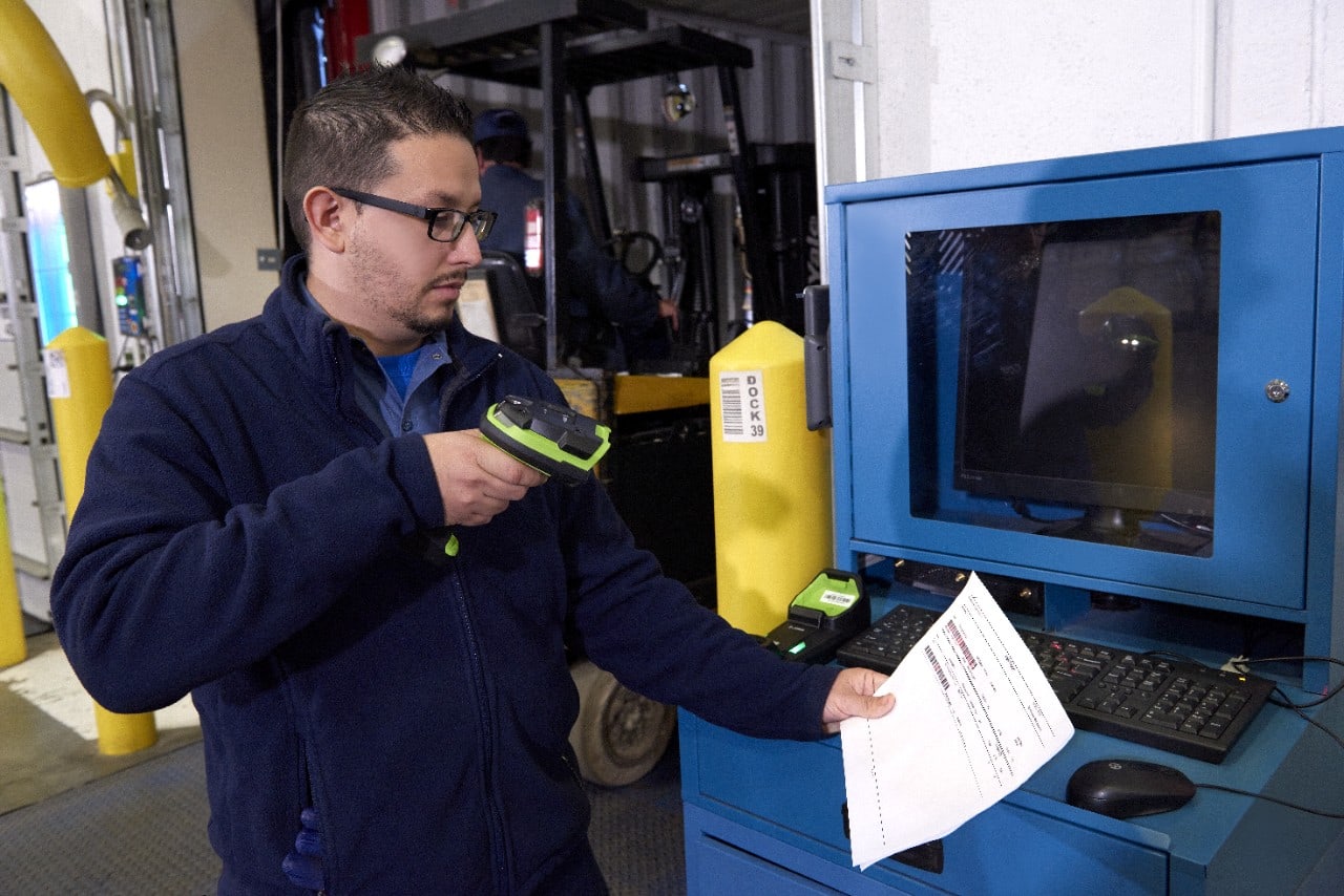 A worker scanning a label with a cordless Zebra scanner beside a shop-floor terminal