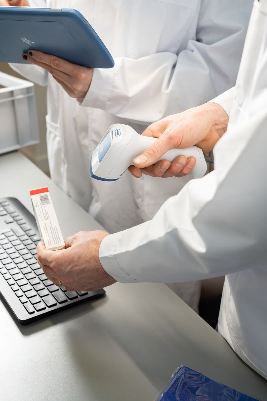 A gloved hand scanning a sample with a Zebra handheld scanner beside a keyboard