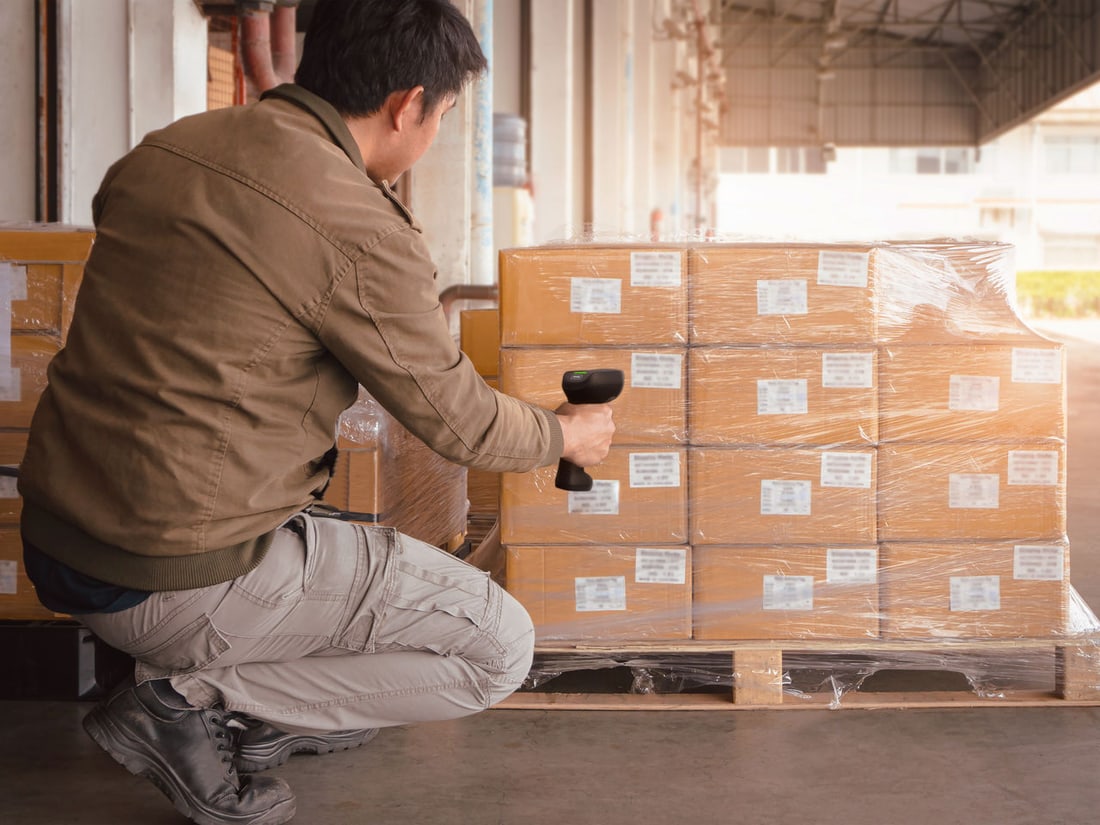 A worker scanning cartons on a stretch-wrapped pallet
