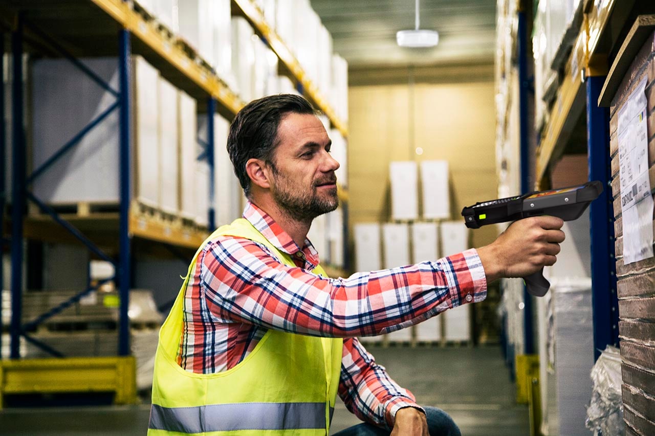 A warehouse worker in a hi-vis vest scanning a rack label with an MC9400