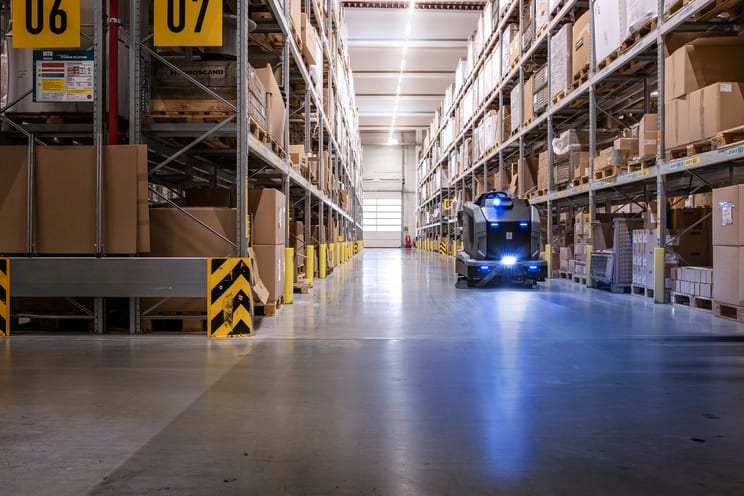 An autonomous floor scrubber cleaning a warehouse aisle