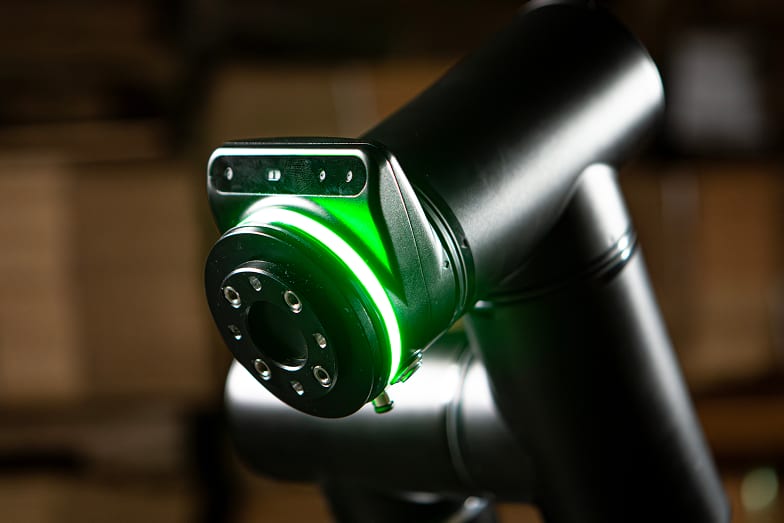 The wrist of a Standard Bots collaborative robot, its vision head lit, in front of stacked cases
